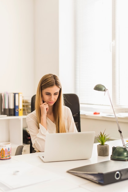 Computer portatile di ricerca portatile affascinante della donna in ufficio