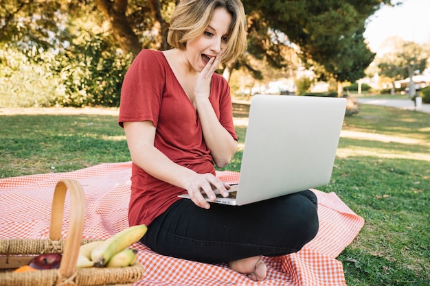 Computer portatile sorpreso di lettura rapida della donna sul picnic