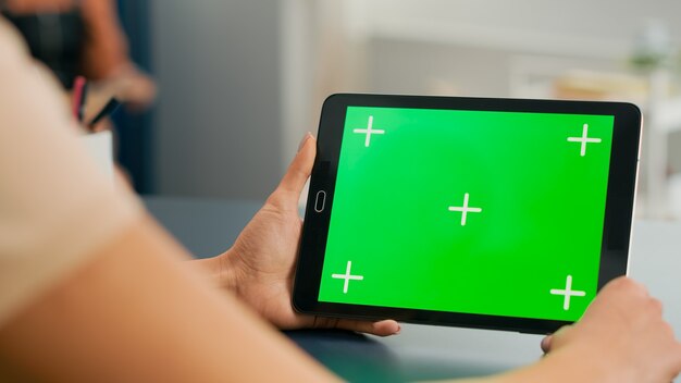 Computer tablet con display chroma key schermo verde mock up in piedi sulla scrivania del tavolo. Donna libera professionista che naviga su un dispositivo isolato per la comunicazione web online nella stanza dell'ufficio domestico