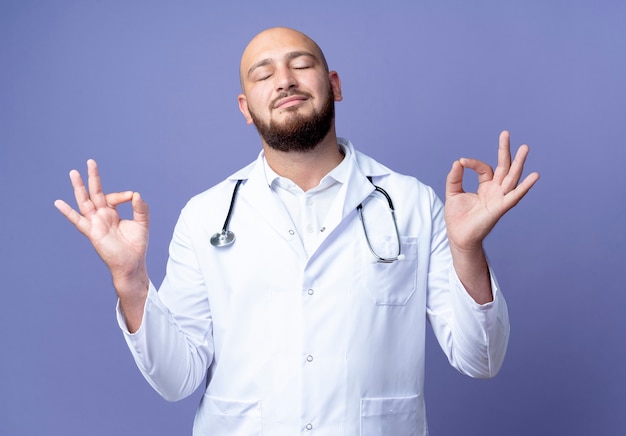 Con gli occhi chiusi giovane medico maschio calvo che indossa veste medica