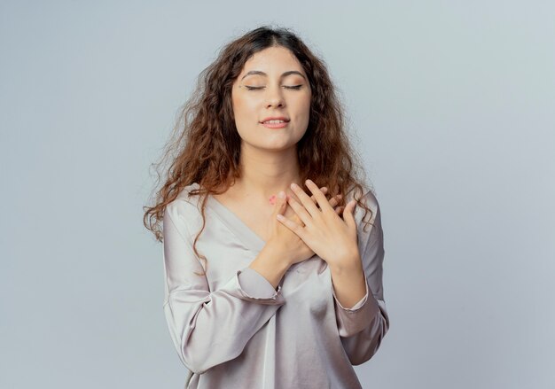 Con gli occhi chiusi soddisfatto giovane impiegato grazioso femminile che mette le mani sul cuore isolato su bianco