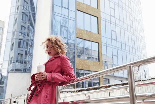 Con i capelli ricci. Una bella donna adulta con un caldo cappotto rosso passeggia in città durante i fine settimana