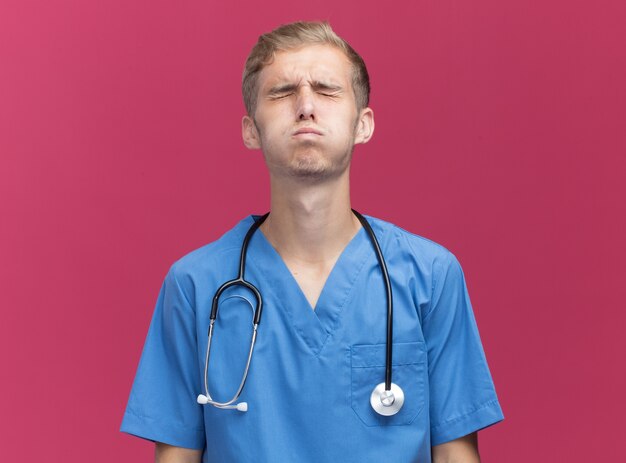 Con il giovane medico maschio di eys chiuso che porta l'uniforme del medico con lo stetoscopio isolato sulla parete rosa