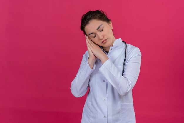 Con la ragazza del medico degli occhi chiusi che indossa l'abito medico e lo stetoscopio che mostra il gesto di sonno su fondo rosso parassitario