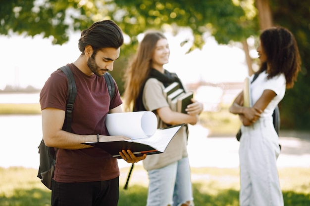 Concentrati su un ragazzo indiano che sta in piedi separatamente. Gruppo di studenti internazionali in piedi insieme nel parco dell'università