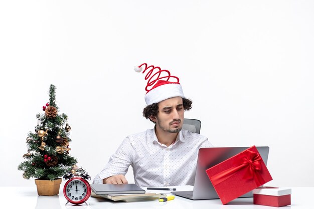 Concentrato giovane imprenditore con buffo cappello di Babbo Natale che celebra il Natale in ufficio su sfondo bianco