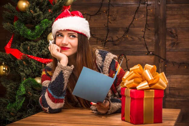 Concetti di Capodanno e Natale. Bella ragazza in possesso di una cartolina di Natale e Capodanno e sorridente. Bei regali in piedi di fronte a lei.