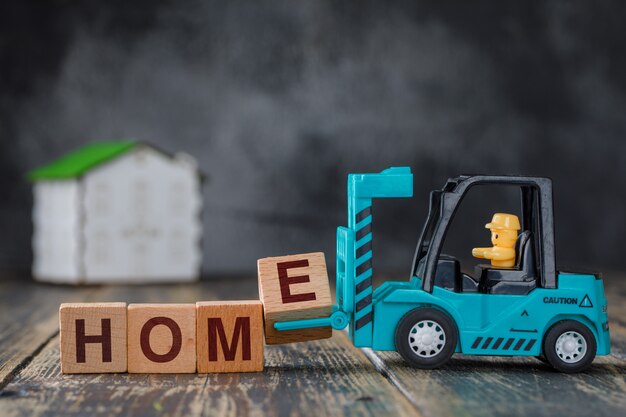 Concetto del bene immobile con la casa di modello sulla vista laterale della tavola di legno. carrello elevatore che trasporta il blocco di lettere e a casa dell'iscrizione.