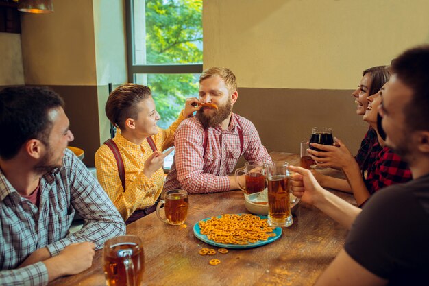 Concetto della gente, di svago, di amicizia e di comunicazione - amici felici che bevono birra, chiacchiere e tintinnio al bar o al pub