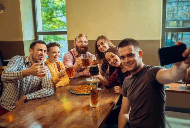 Concetto della gente, di svago, di amicizia e di comunicazione - amici felici che bevono birra, chiacchiere e tintinnio al bar o al pub