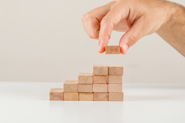 Concetto della gestione dei rischi e di affari sulla vista laterale del backgroud bianco. uomo d'affari ponendo blocco di legno sulla torre.