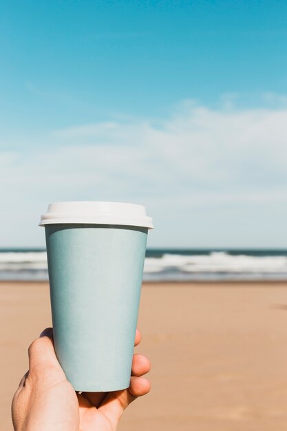 Concetto della spiaggia con la tazza di carta della tenuta della mano