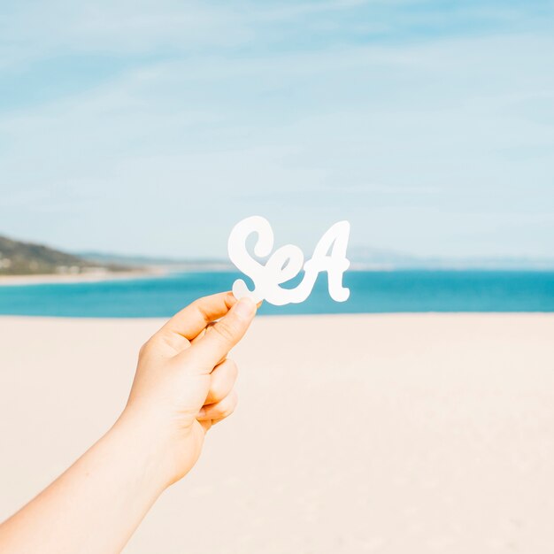 Concetto della spiaggia con le mani che tengono le lettere del mare