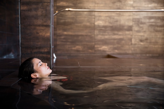 Concetto della stazione termale con la donna che si distende in acqua