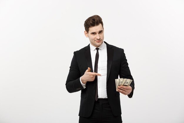 Concetto di affari: bell'uomo d'affari in tuta che punta il dito sui soldi. Isolato su sfondo bianco.