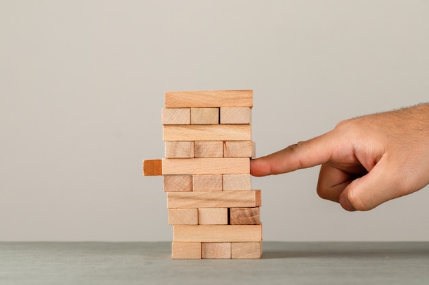 Concetto di affari e di rischio e della gestione sulla vista laterale della parete grigia e bianca. dito che spinge la torre del blocco di legno.