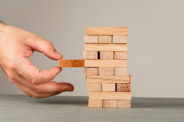 Concetto di affari e di rischio e della gestione sulla vista laterale della parete grigia e bianca. mano estraendo il blocco di legno.