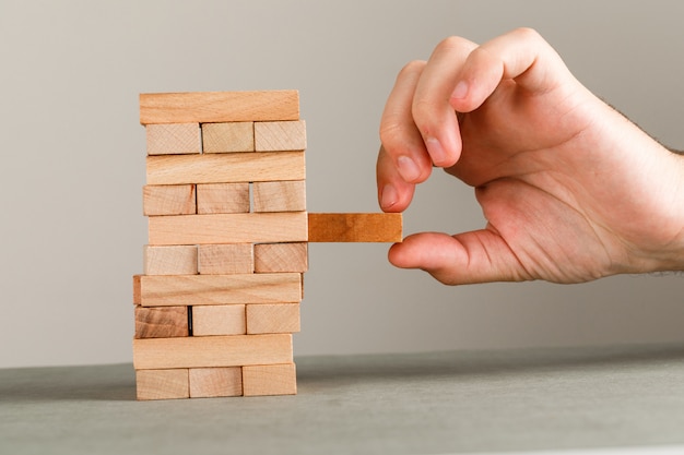 Concetto di affari e di rischio e della gestione sulla vista laterale della parete grigia e bianca. mano estraendo il blocco di legno.