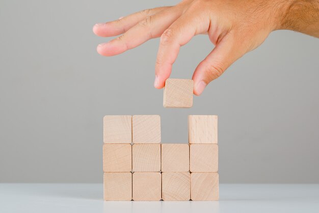 Concetto di affari sulla vista laterale della tavola bianca e grigia. mano tirando o posizionando il cubo di legno.