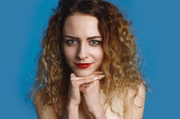 Concetto di bellezza, stile, moda e femminilità. Foto di stupefacente giovane donna dagli occhi blu caucasica con trucco e manicure tenendo le mani sotto il mento, guardando con calma sorriso soddisfatto