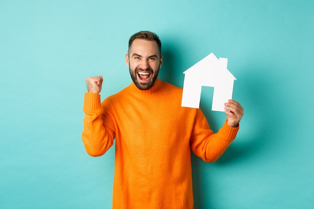 Concetto di bene immobile. Uomo eccitato che dice di sì, che mostra il maket della casa di carta e che sembra soddisfatto