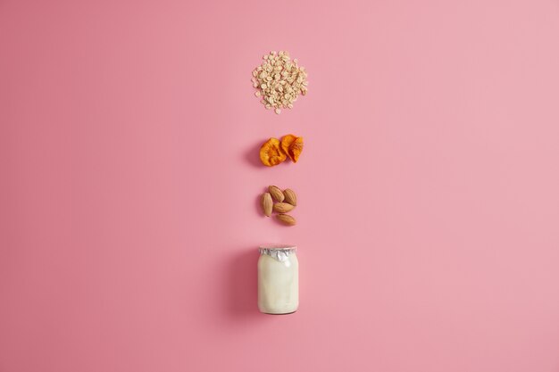 Concetto di cibo dieta sana. Vasetto di vetro di yogurt fresco, cereali d'avena, albicocche secche e mandorle noci per preparare la colazione. Nutrizione appropriata. Ingredienti per preparare deliziosi fiocchi d'avena fatti in casa