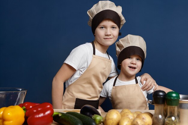 Concetto di cibo e nutrizione. Colpo isolato di due fratelli germani allegri ragazzini in posa in cucina