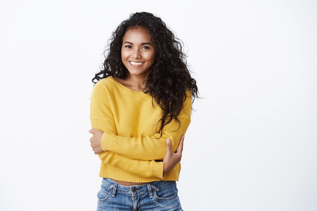 Concetto di comfort, romanticismo e intimità. Allegra bella ragazza afro-americana in maglione giallo che si abbraccia, abbracciando il corpo come sentirsi a proprio agio macchina fotografica sciocca sorridente sul muro bianco