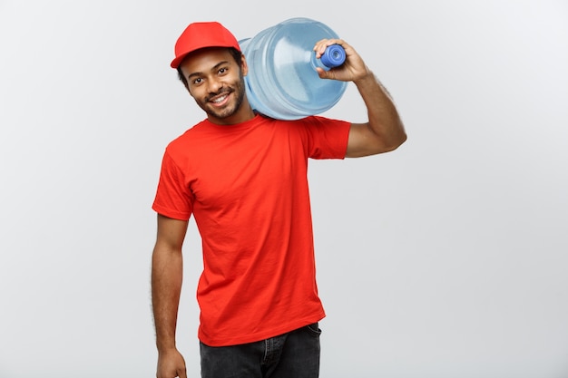 Concetto di consegna - bello uomo africano di consegna uomo che detiene serbatoio d&#39;acqua. Isolato su sfondo grigio dello studio. Copia spazio.