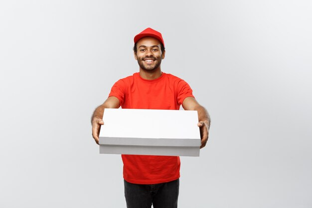 Concetto di consegna - Ritratto di bello uomo di consegna pizza afroamericana. Isolato su sfondo grigio dello studio. Copia spazio.