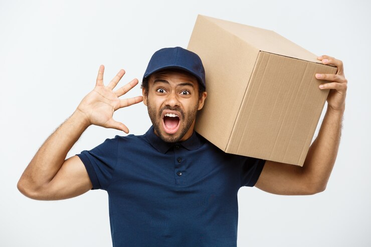 Foto gratuito concetto di consegna - ritratto di serio uomo di consegna afro-americano mostrando espressione sciocca aggressiva con la tenuta di un pacchetto di scatola. isolato su sfondo grigio dello studio. copia spazio.