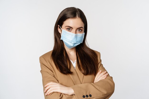 Concetto di coronavirus e pandemia. Donna d'affari professionista, impiegata in maschera medica con le braccia incrociate sul petto, con un aspetto sicuro, sfondo bianco