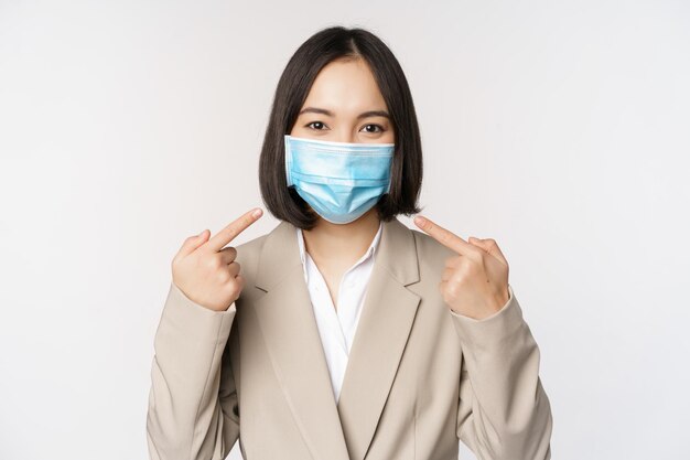 Concetto di coronavirus e uomini d'affari Imprenditrice asiatica che punta il dito sulla maschera medica sul posto di lavoro in piedi su sfondo bianco