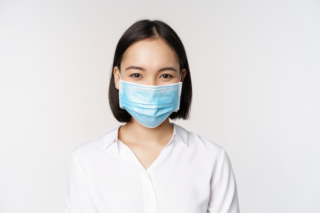 Concetto di Covid e assistenza sanitaria Ritratto ravvicinato della donna asiatica dell'ufficio in maschera facciale che sorride utilizzando la protezione dal coronavirus durante la pandemia sfondo bianco