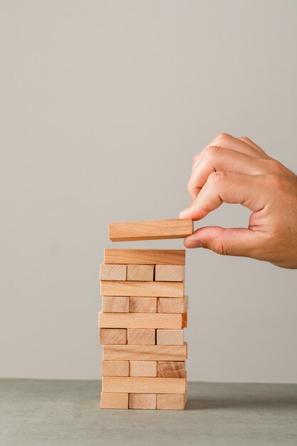 Concetto di crescita di affari sulla vista laterale della parete grigia e bianca. mano mettendo il blocco di legno sulla torre.