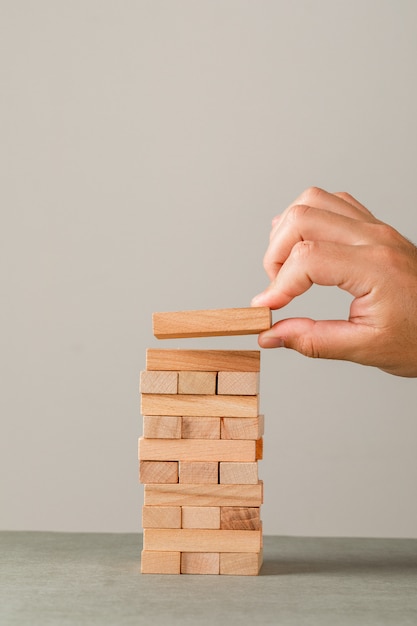 Concetto di crescita di affari sulla vista laterale della parete grigia e bianca. mano mettendo il blocco di legno sulla torre.