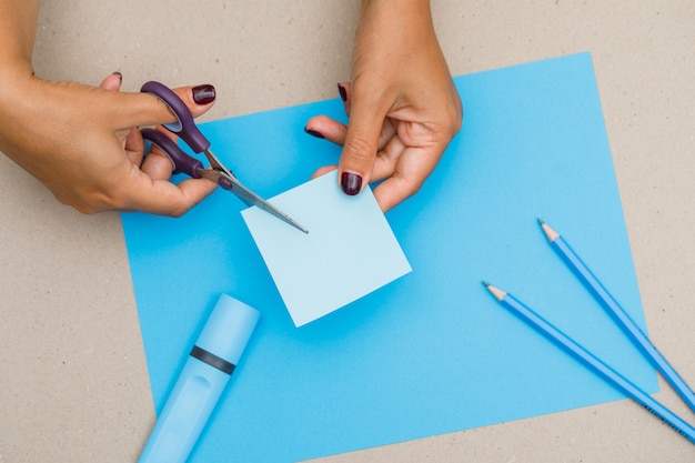 Concetto di educazione con materiale scolastico su carta, piatto laici. donna che taglia nota appiccicosa.