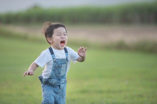 Concetto di estate, infanzia, tempo libero e persone - ragazzino felice che gioca a correre all'aperto sul campo verde. Ragazzo carino che attraversa l'erba e sorride.