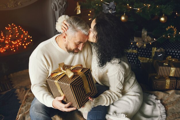 Concetto di età e persone. Coppia senior con confezione regalo su sfondo di luci. Donna in una felpa lavorata a maglia bianca.