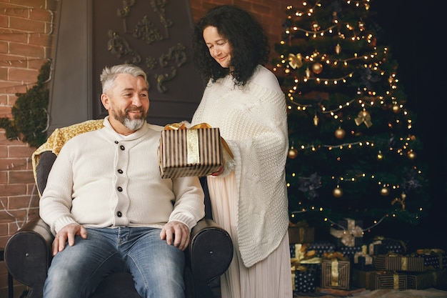 Concetto di età e persone. Coppia senior con confezione regalo su sfondo di luci. Donna in una felpa lavorata a maglia bianca.