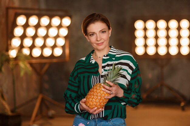 Concetto di fitness, casa e dieta. Ananas della tenuta della giovane donna che sta al tavolo da cucina