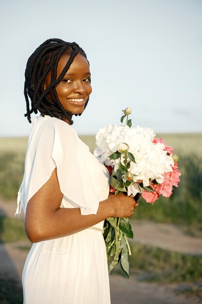 Concetto di giornata internazionale della donna. Felice giovane donna afroamericana con un mazzo di fiori di peonia.