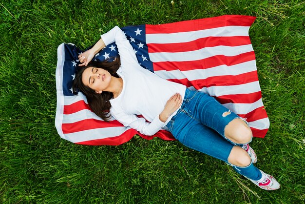 Concetto di giorno di indipendenza con la donna che si trova giù sulla bandiera americana