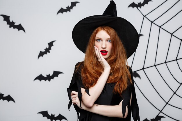 Concetto di Halloween - Bella strega caucasica scioccante con qualcosa sul muro grigio.