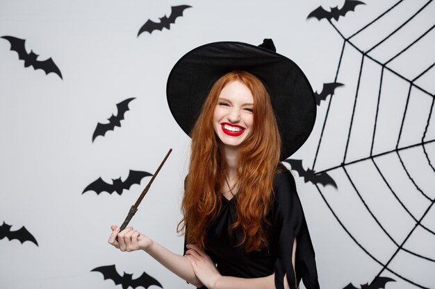 Concetto di Halloween - Bella strega che gioca con il bastone magico sulla parete grigia.
