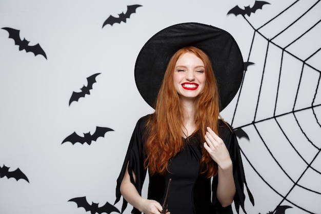 Concetto di Halloween - Bella strega che gioca con il bastone magico sulla parete grigia.