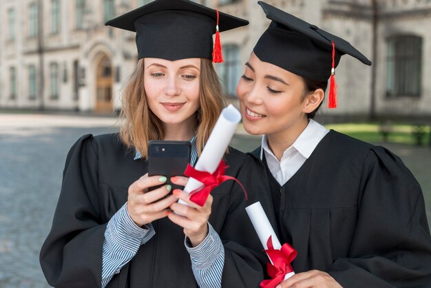Concetto di laurea con gli studenti guardando smartphone