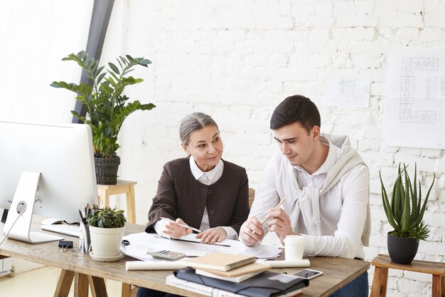 Concetto di lavoro di squadra, cooperazione e collaborazione. Team di ingegnere donna anziana che aiuta il suo giovane apprendista maschio abile, dandogli consigli, condividendo esperienze, visione e idee creative