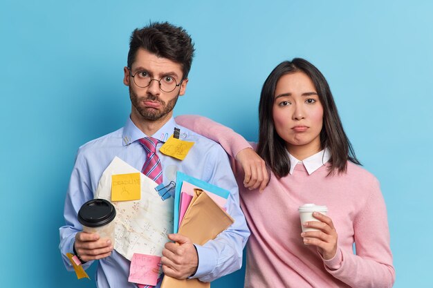 Concetto di lavoro di squadra. Due colleghi stanchi scontenti hanno preparato la relazione finanziaria insieme posano con il caffè per andare a guardare tristemente la fotocamera. Gli studenti hanno una scadenza per preparare l'esame finale all'università