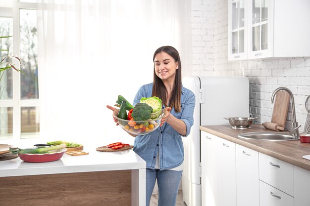 Concetto di mangiare sano. Giovane bella donna in cucina con frutta e verdura